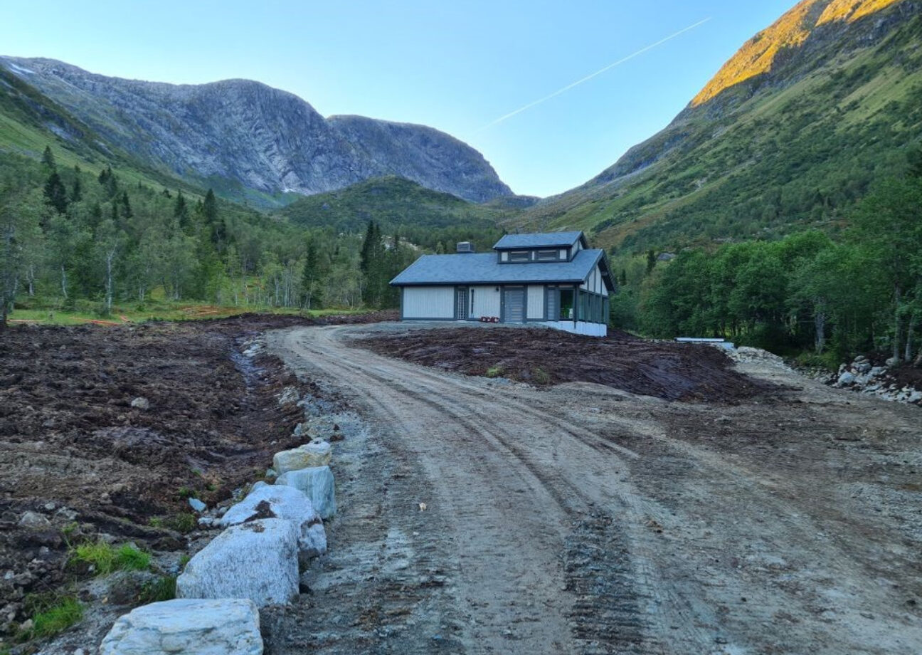 En grusvei med Kupe kraftverk i fokus, og fjell rundt kraftverket.
