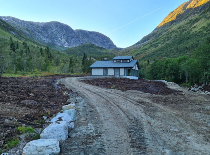 En grusvei med Kupe kraftverk i fokus, og fjell rundt kraftverket.